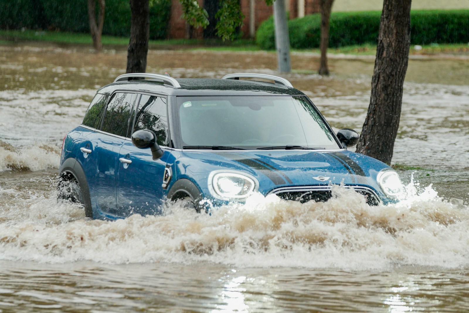 A blue car driving through a flooded street